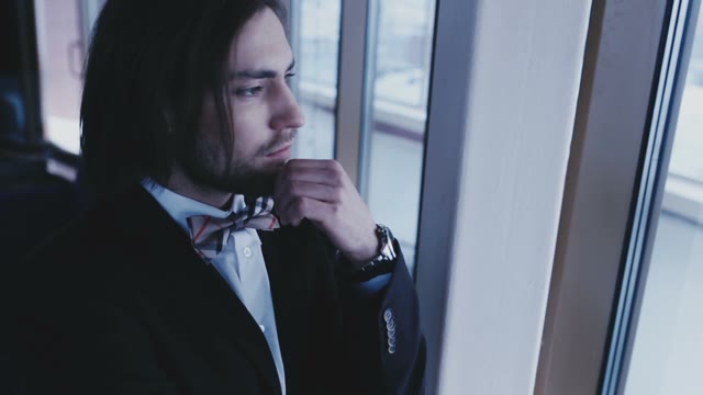 The Groom In A Bow Tie, Is Looking From Side To Side In Front Of The Window