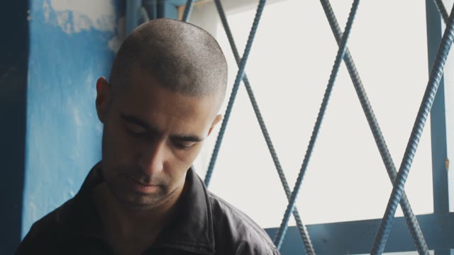 Pensive And Sad Prisoner Sitting At The Lattice Window