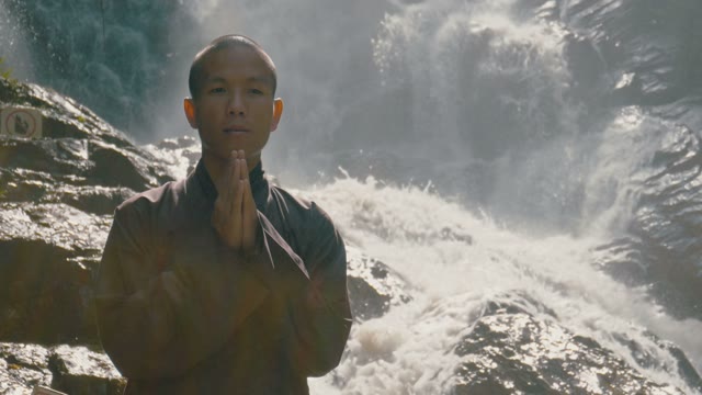 Monk Stands Near The Waterfall Close-up