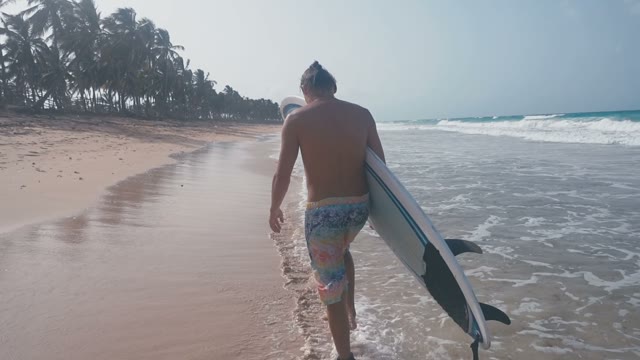A Beautiful Surfer Walks Along The Beach Which Is Washed By Waves