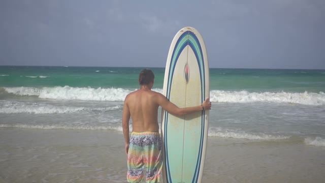 A Young Handsome Surfer Is Standing On The Shore