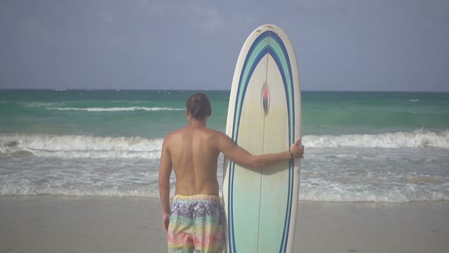 Young Handsome Surfer With A Good Physique Stands On The Beach