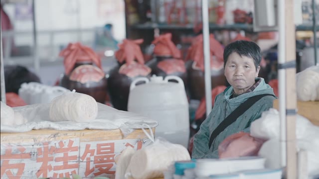 Chinese Woman Sitting On A Market Surrounded By Heaps Of Bags