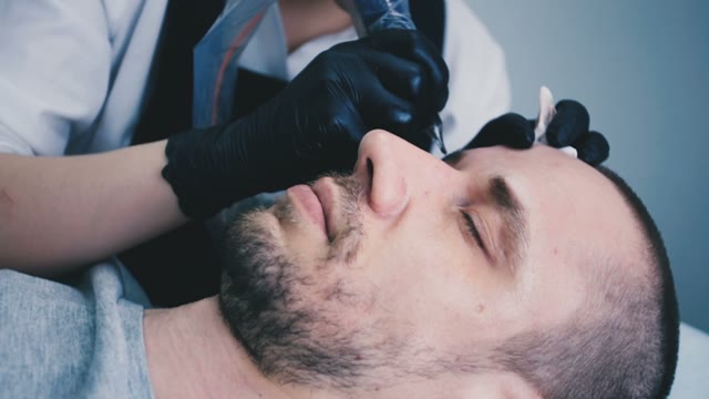 Woman Does Tattoo Of Man's Eyebrows Close-up