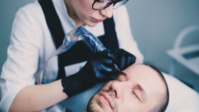 Woman Does Tattoo Of Man's Eyebrows Close-up