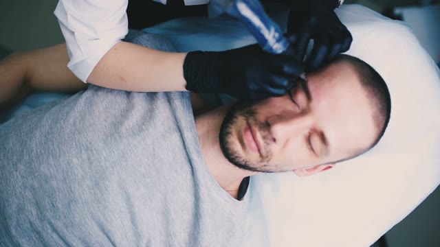 Woman Does Tattoo Of Man's Eyebrows Close-up