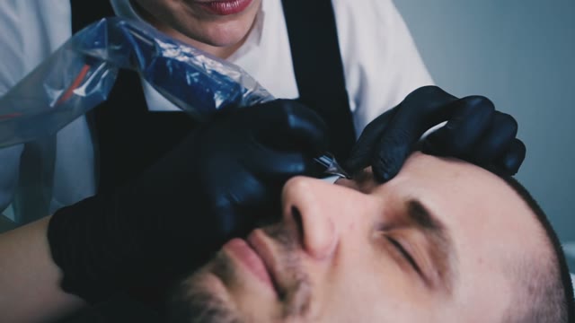 Woman Does Tattoo Of Man's Eyebrows Close-up