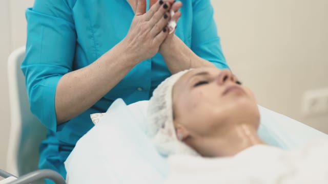 The Employee Of The Spa Salon Applies An Ennobling Cream On The Face Of A Young