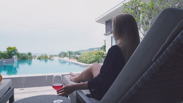 Beautiful Girl Sits By The Pool With A Glass In Hands