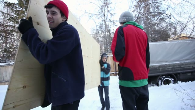 Young People Unload A Car With Plywood