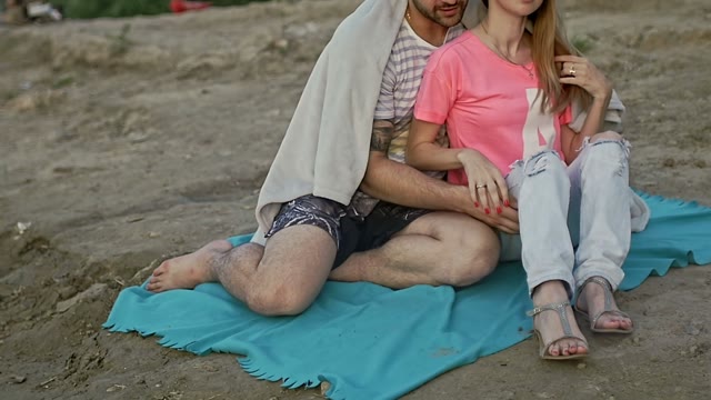 Young Couple Sitting On The Beach Hiding Behind A Blanket