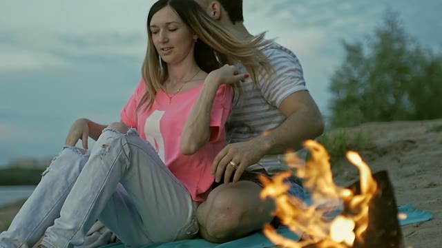 Young Couple Sitting By The Fire On The Coast