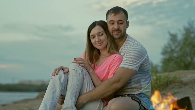 Guy And A Girl Are Sitting On The Shore Looking At The Bonfire